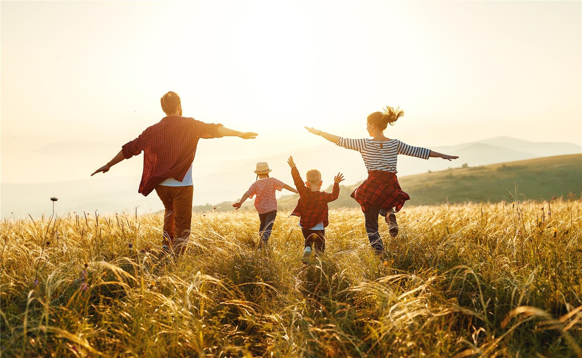 Familie läuft durch eine Graslandschaft und breitet die Arme aus