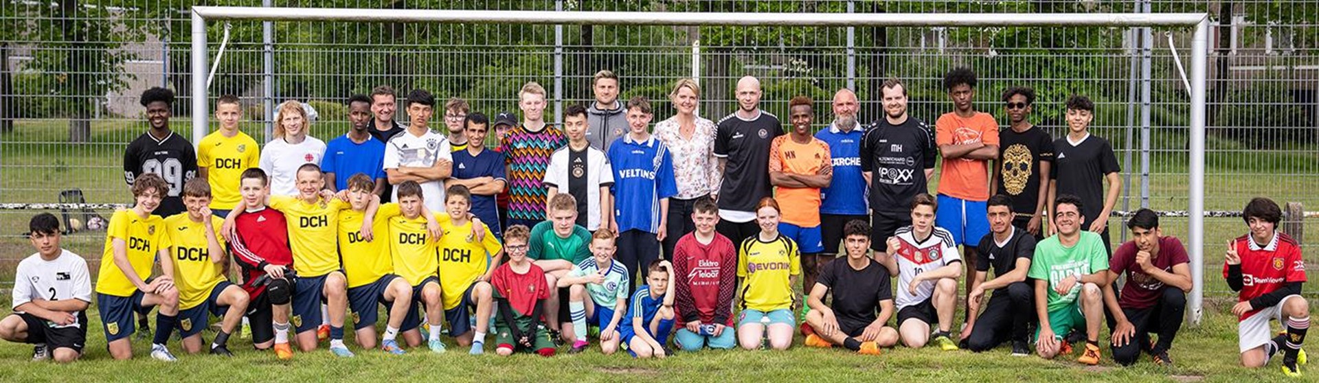 eine Gruppe von Personen vor einem Fußballtor auf einem grasbewachsenen Spielfeld