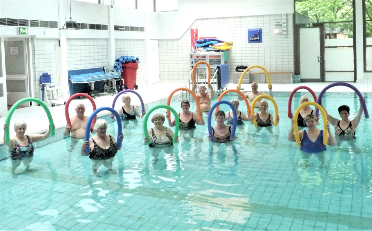 Ältere Menschen in einem Schwimmbecken mit einer Schwimmnudel in den Händen