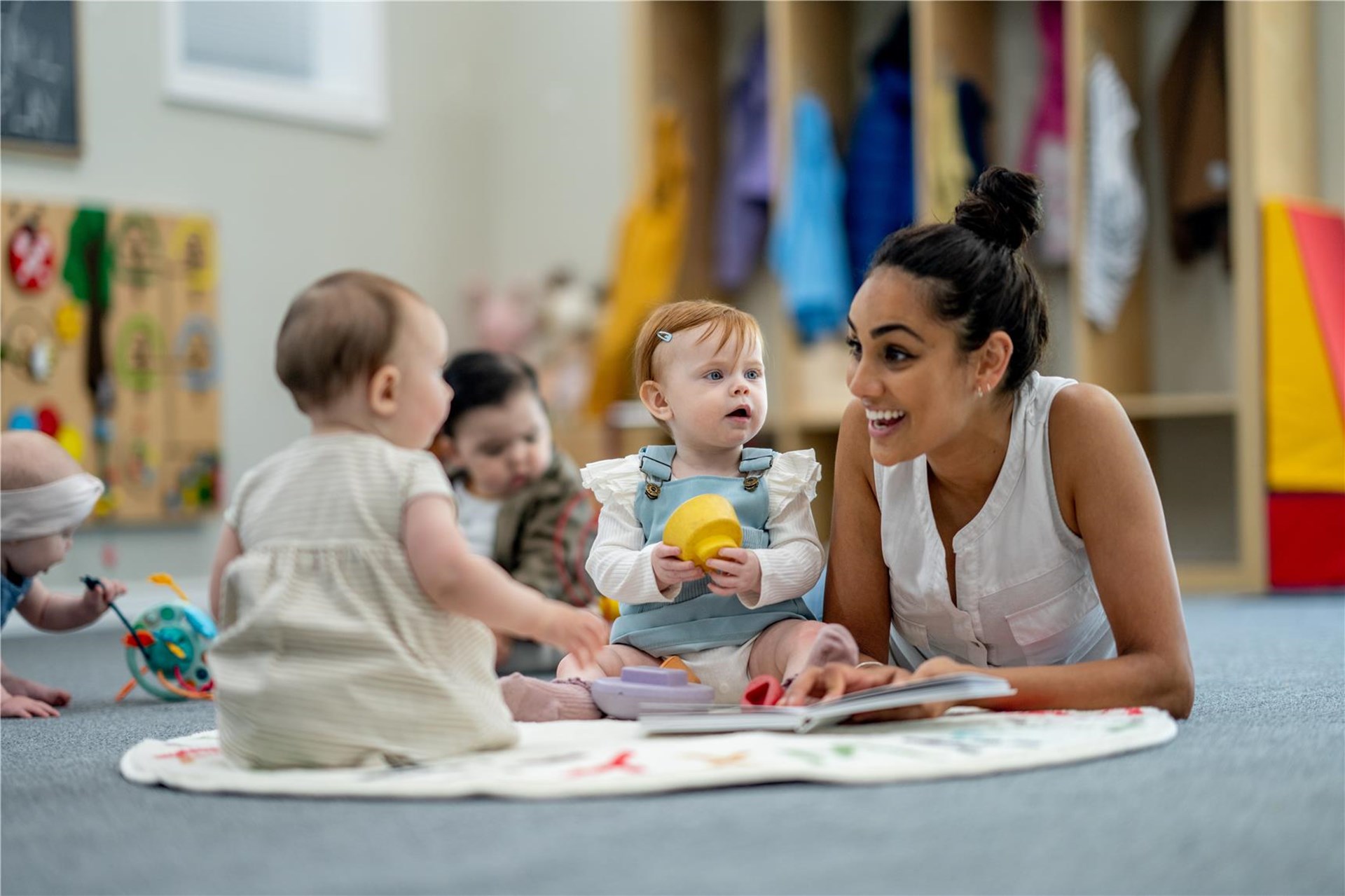 Drei kleine Kinder sitzen gemeinsam mit einer erwachsenen Person auf dem Boden.