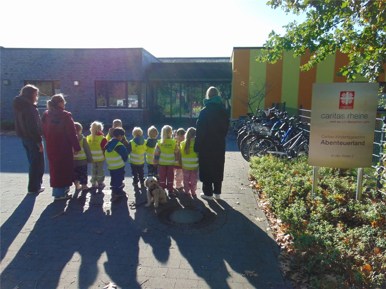 Drei Erwachsene und mehrere Kinder stehen vor einem Flachdach-Gebäude.