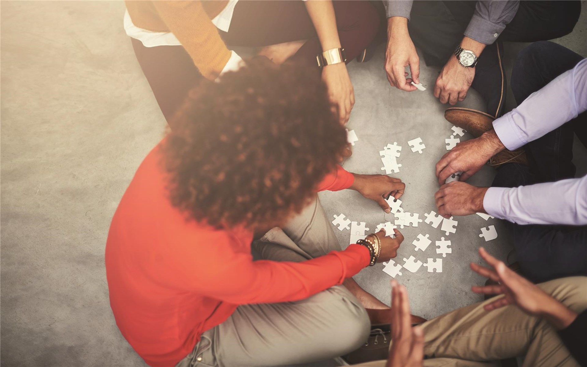 Mehrere Personen sitzen im Kreis auf dem Boden und puzzlen.