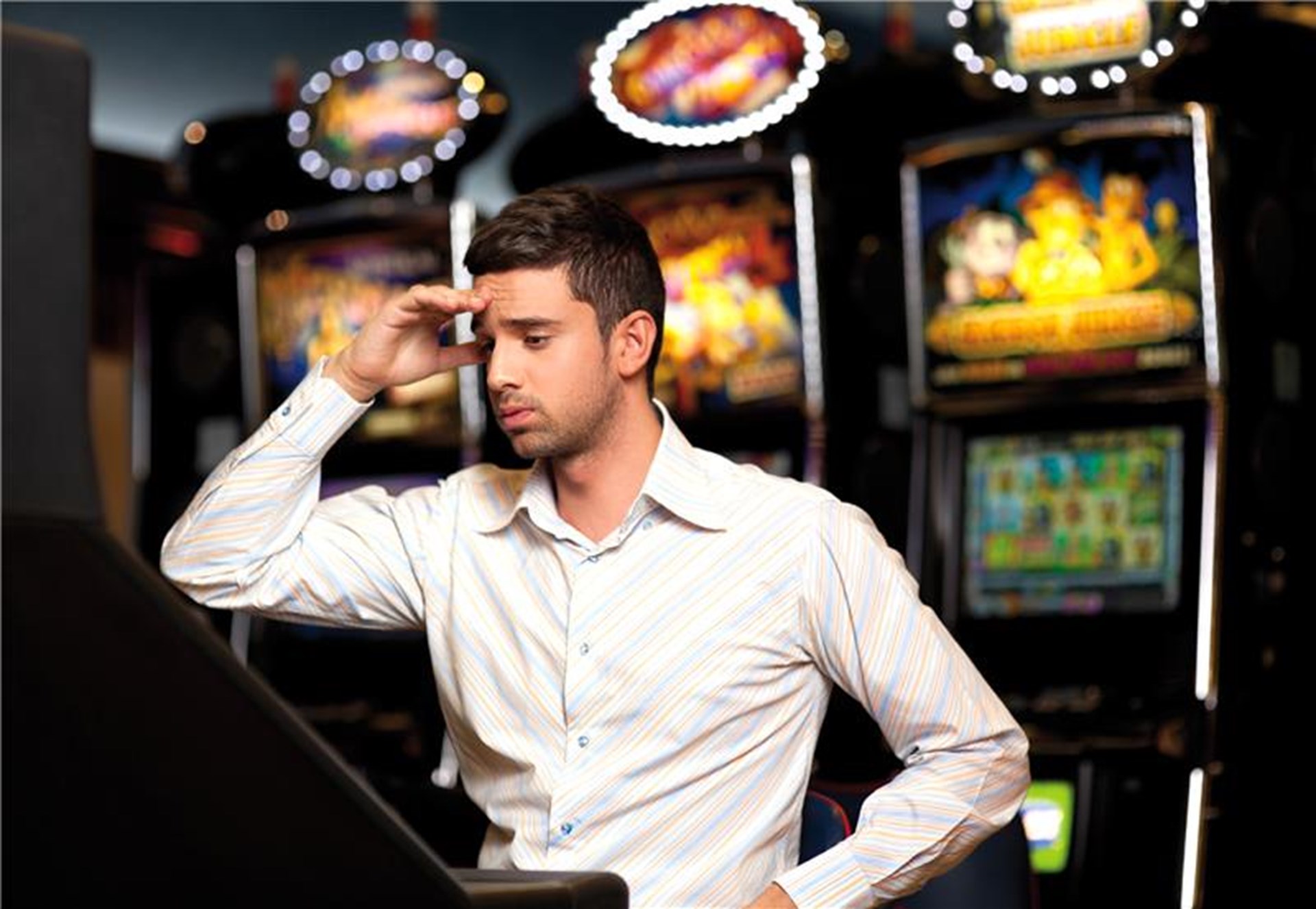 Mann am Spielautomaten. Der Mann hält sich besorgt die Hand an die Stirn.