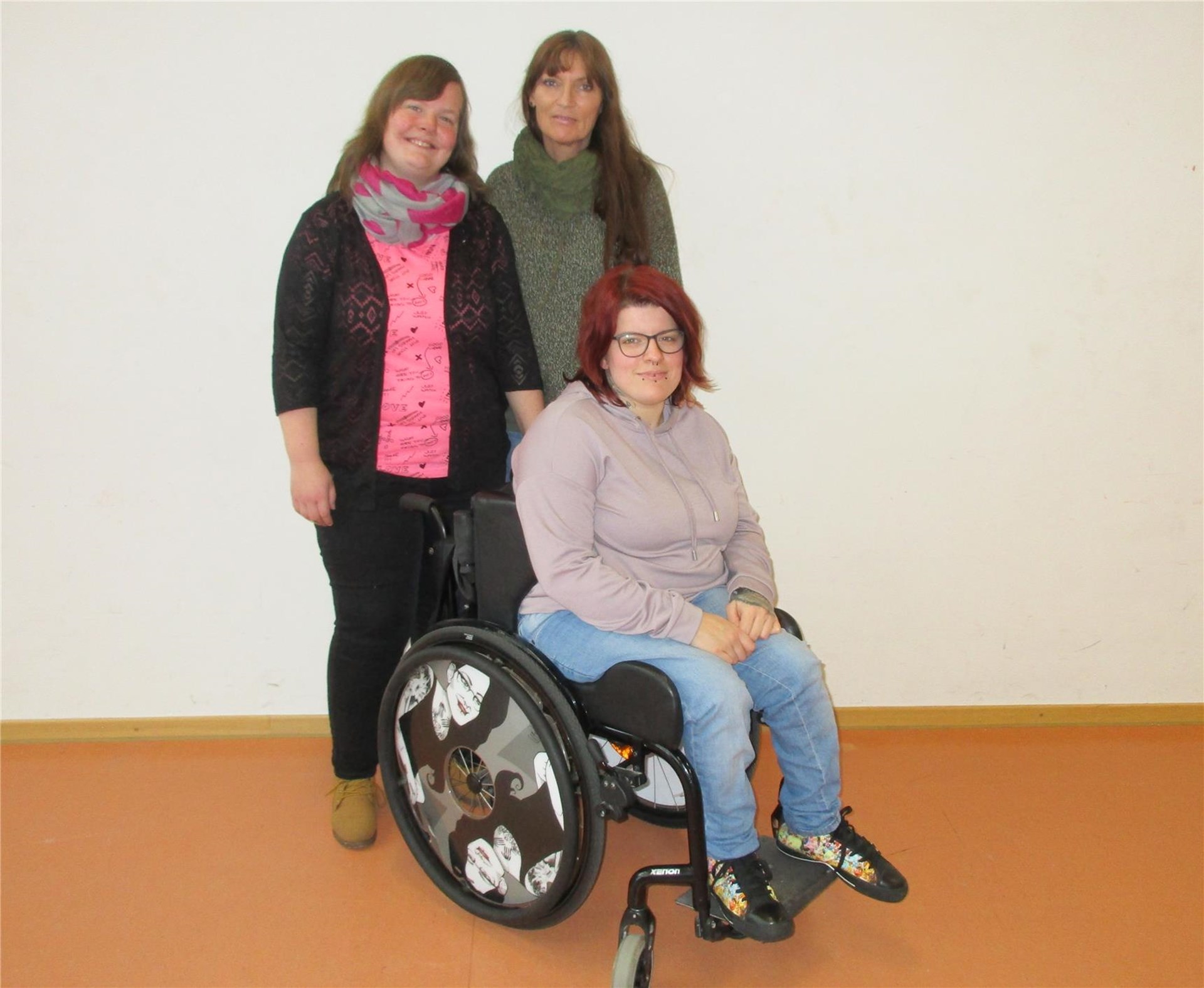 Eine Frau sitzt im Rollstuhl, zwei weitere Frauen stehen dahinter