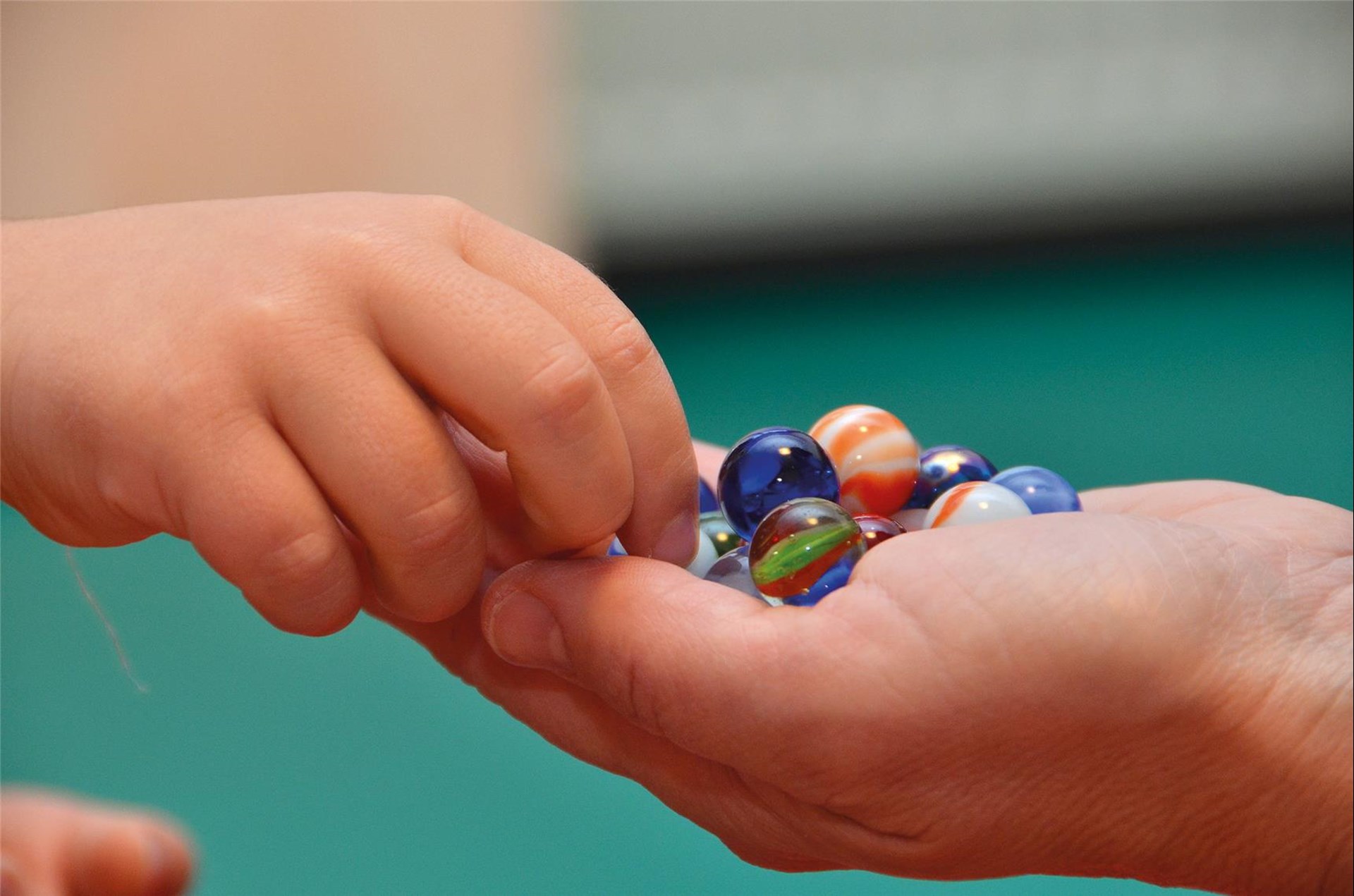 Eine Hand hält Murmeln in offener Handfläche, ein Kinderhand nimmt sich eine davon
