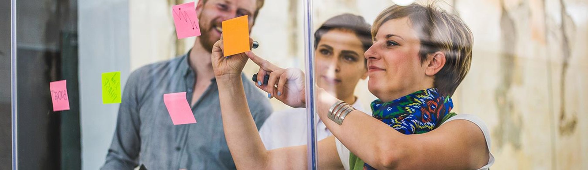 Zwei Frauen und ein Mann kleben Postit-Zettel an eine Glasscheibe