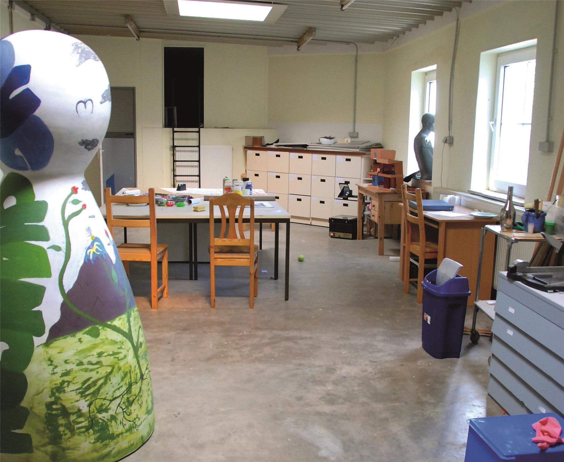 Räumlichkeiten der Jugend- und Kreativwerkstatt, Tische, Stühle und Aufbewahrungsmöglichkeiten. Im Vordergrund ist eine Skulptur zu sehen.