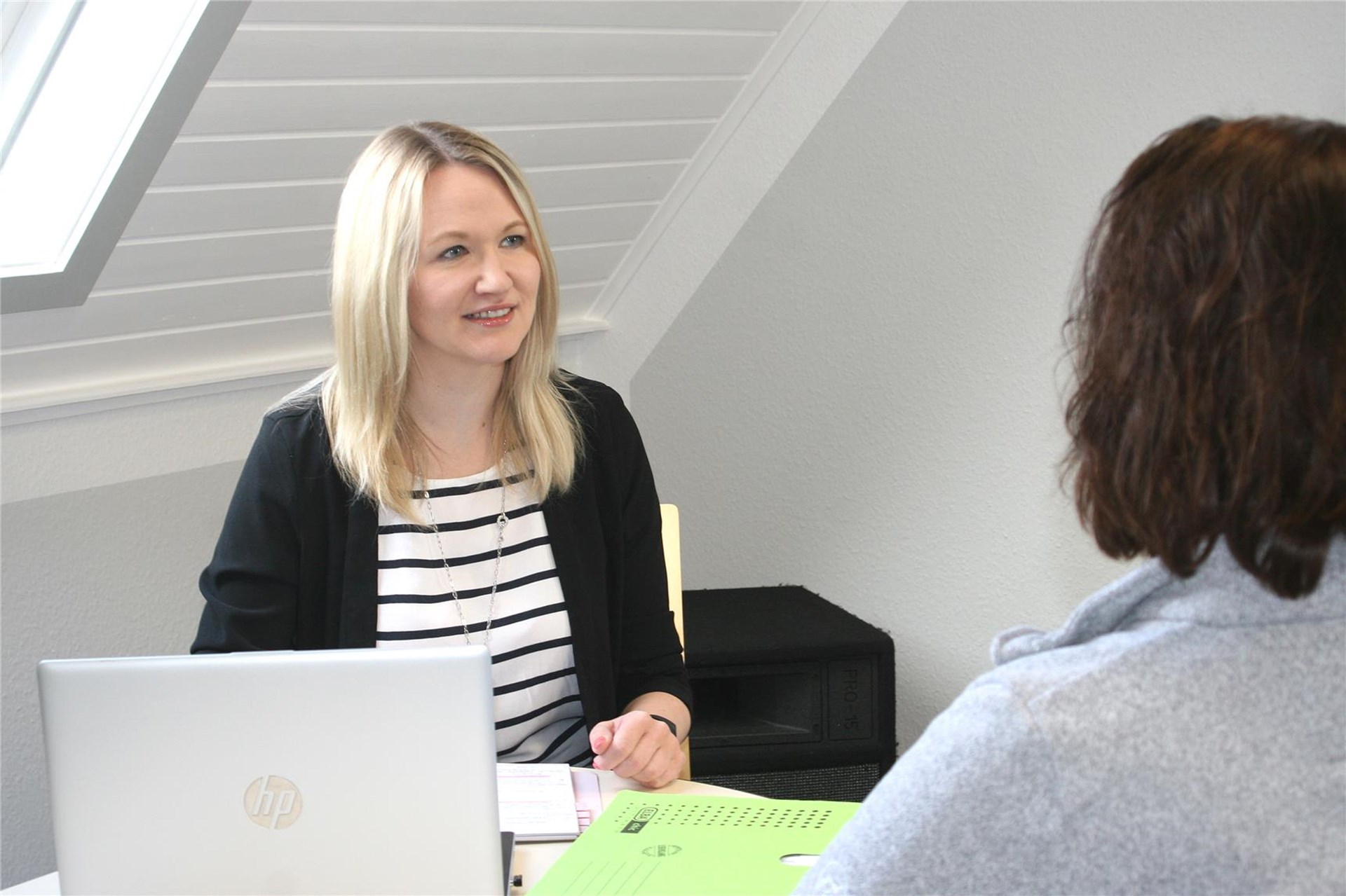 Eine junge Frau sitzt hinter einem Schreibtisch, eine weitere sitzt auf der anderen Seite